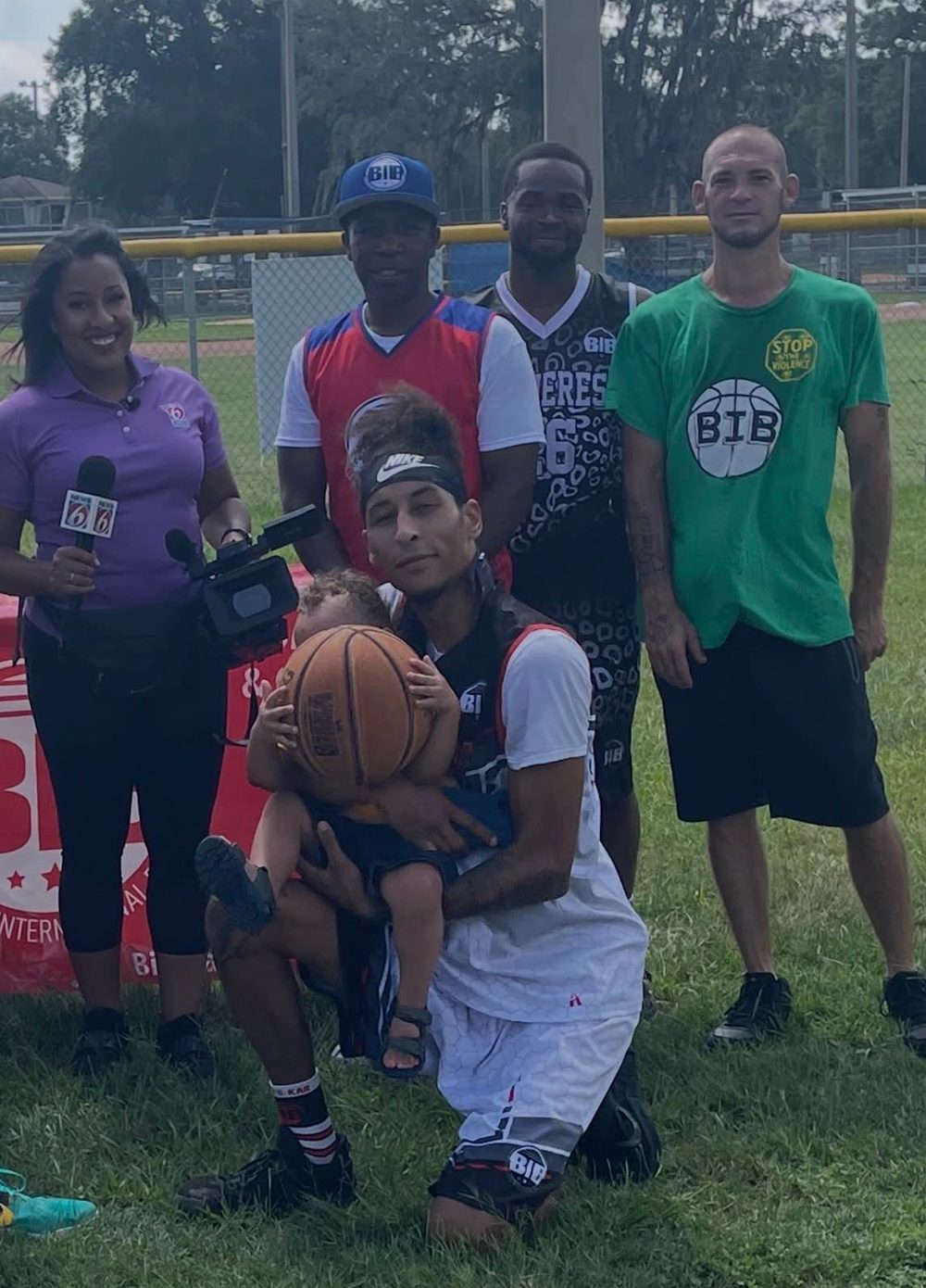 News 6 reporter on the court with B.I.B players and families, one player holding his baby